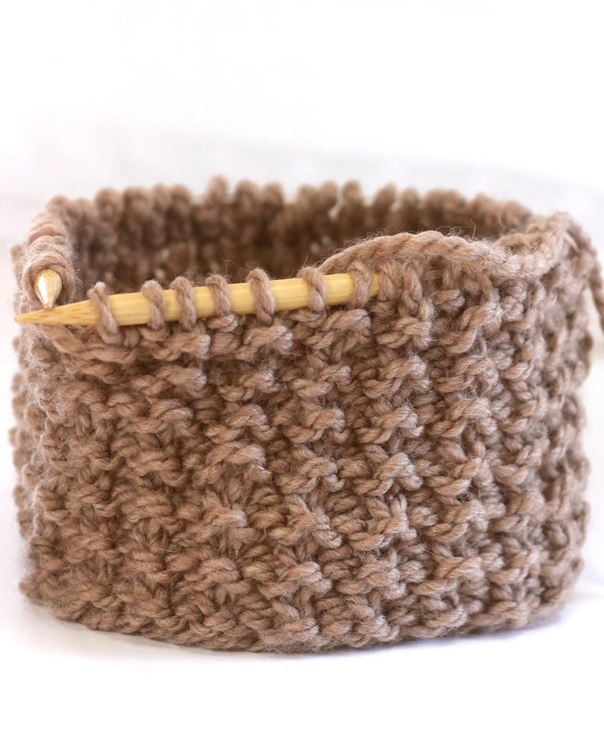 Sand stitch knitting texture on circular bamboo needles with light brown colored yarn.