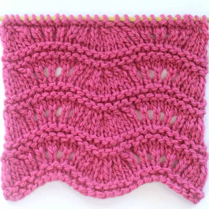 Ripple Ridge knit stitch texture in bulky weight dark pink colored yarn on a wooden bamboo knitting needle.
