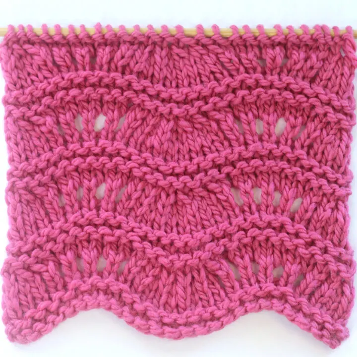 Ripple Ridge knit stitch texture in bulky weight dark pink colored yarn on a wooden bamboo knitting needle.