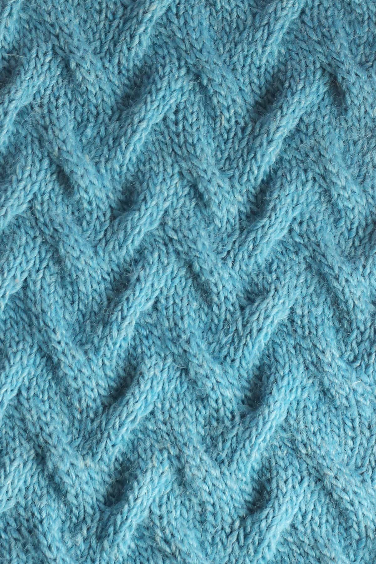 Close up of the Sand Cable knit stitch texture in blue yarn color.