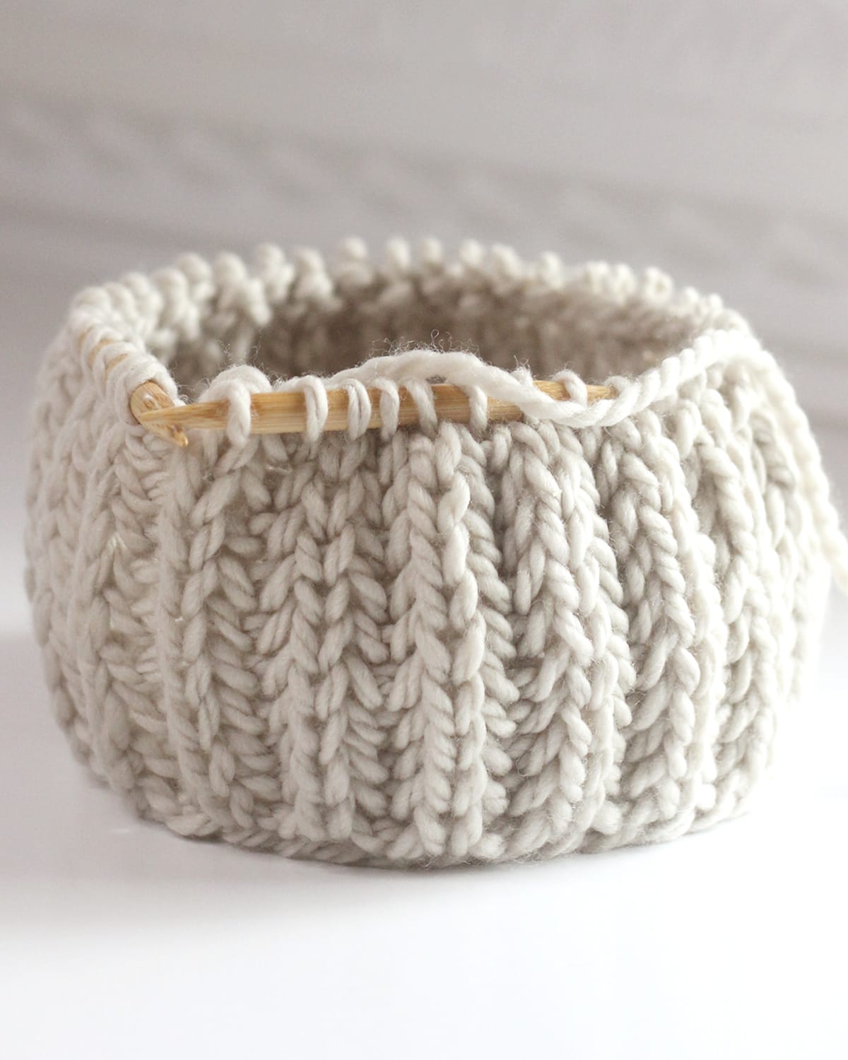 Fisherman's Rib knit stitch texture on circular wooden bamboo needles with beige colored yarn.