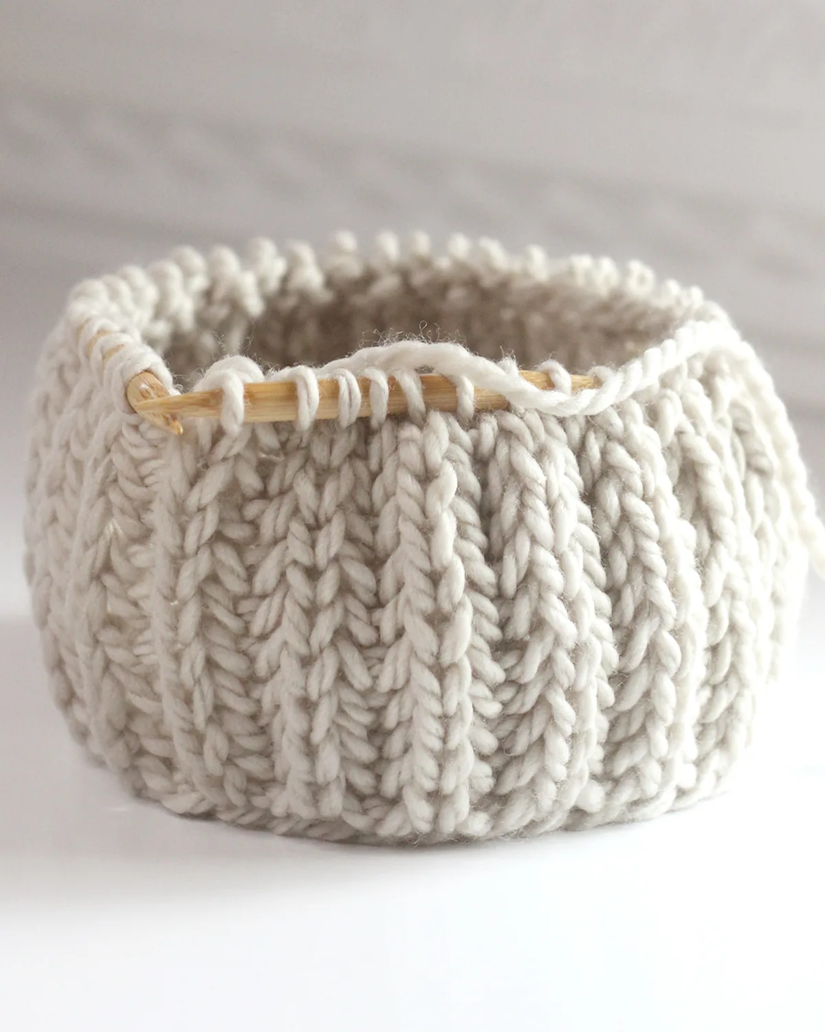 Fisherman's Rib knit stitch texture on circular wooden bamboo needles with beige colored yarn.