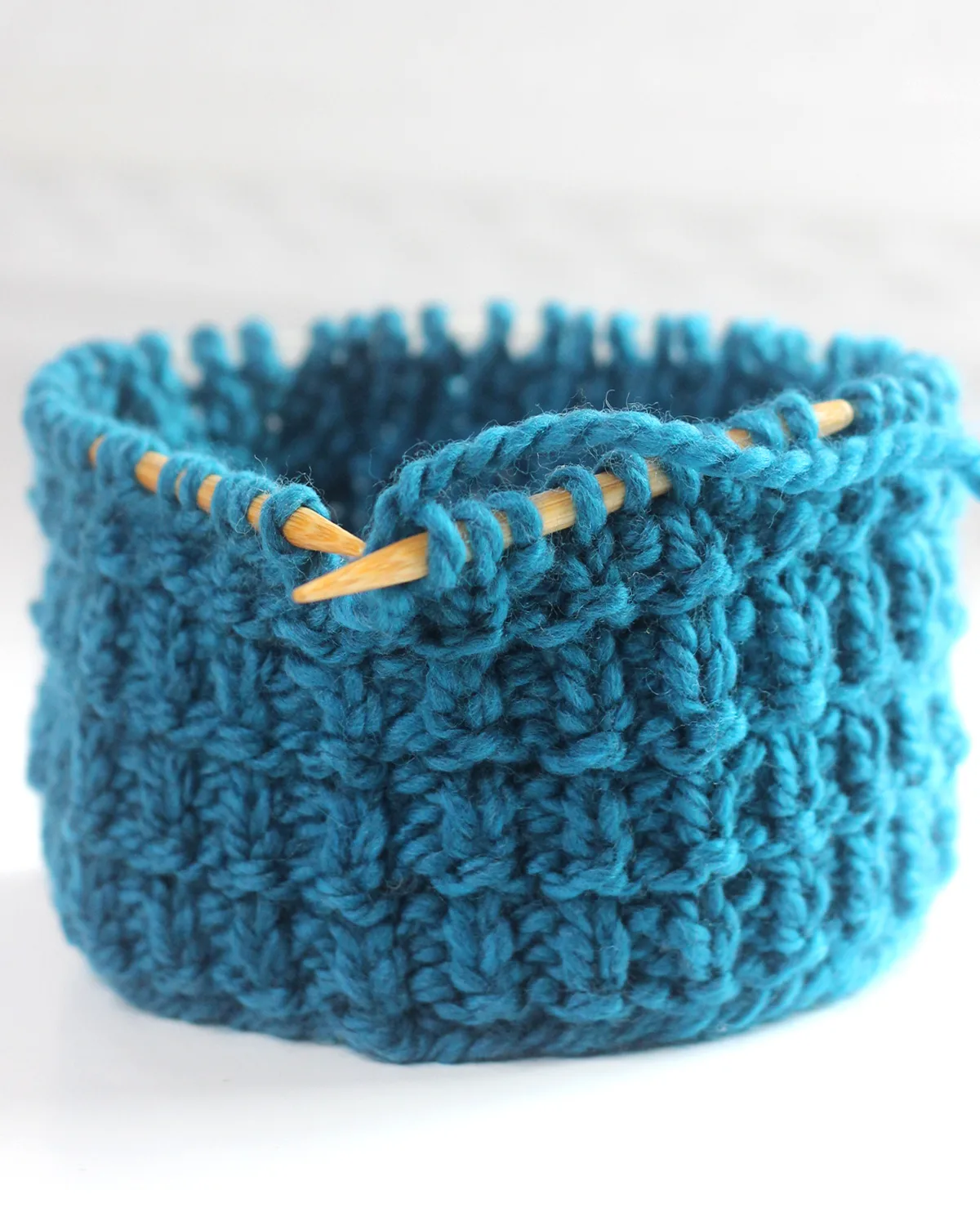 Hurdle stitch knitting texture on circular bamboo needles with blue colored yarn.