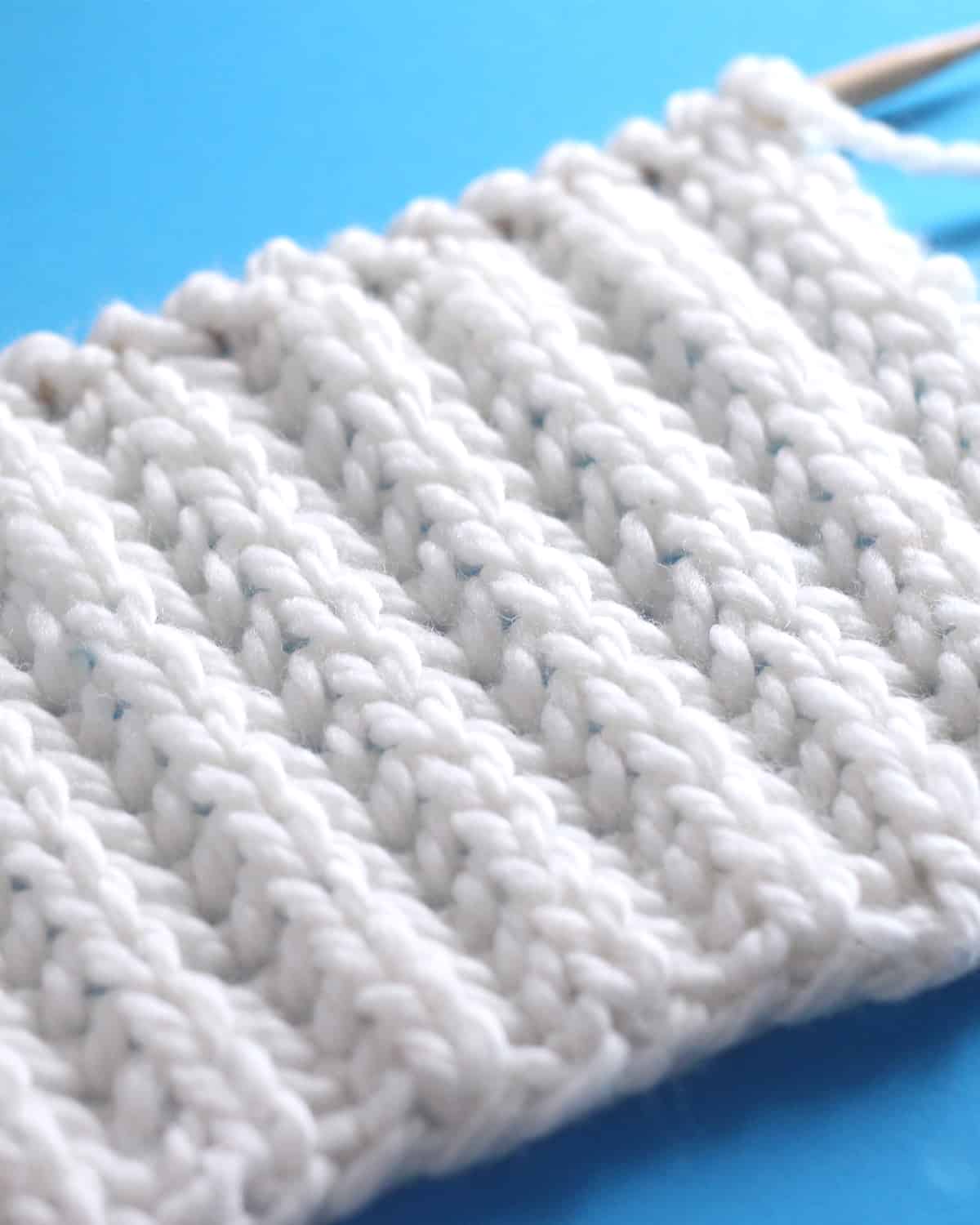Side view close-up of Fisherman's Rib knit stitch pattern with white color yarn on on a wooden bamboo knitting needle.