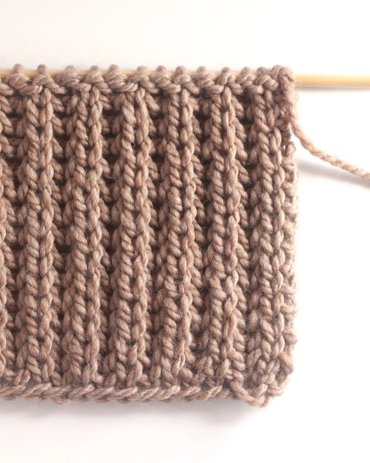 Fisherman's Rib knit stitch pattern in brown yarn color on a wooden bamboo knitting needle by Studio Knit.