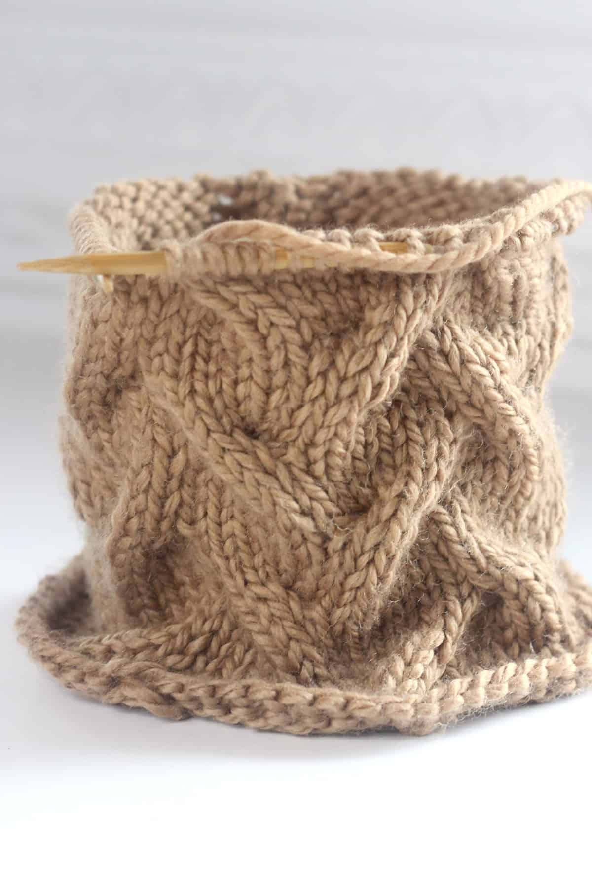 Sand Cable knit stitch texture on circular wooden bamboo needles with brown colored yarn.