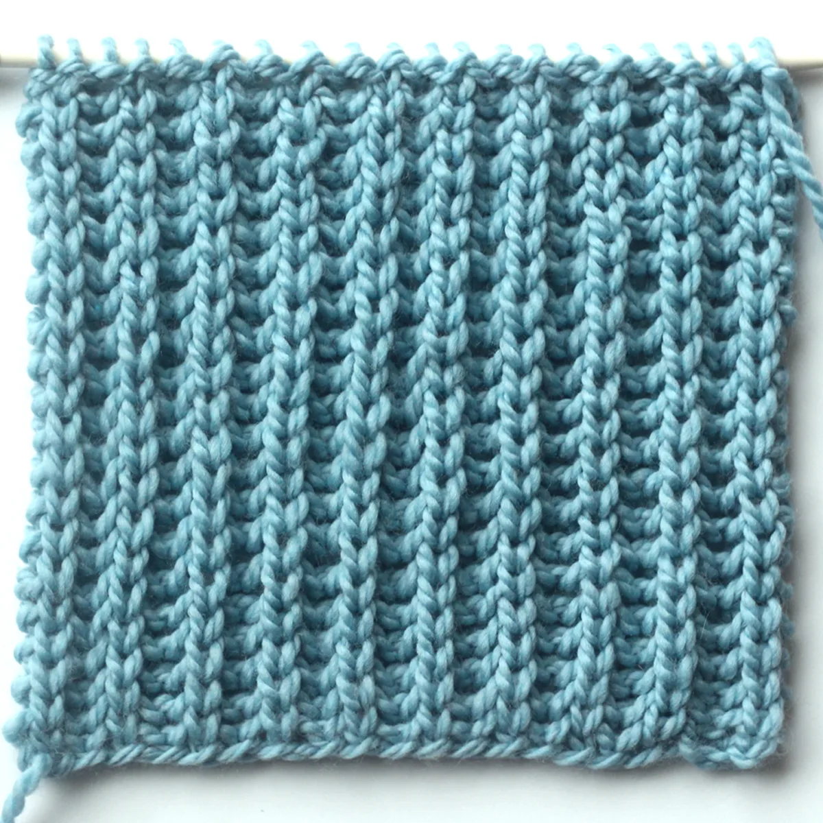 Fisherman's Rib knit stitch pattern knitted flat with a straight knitting needle in light blue yarn color.