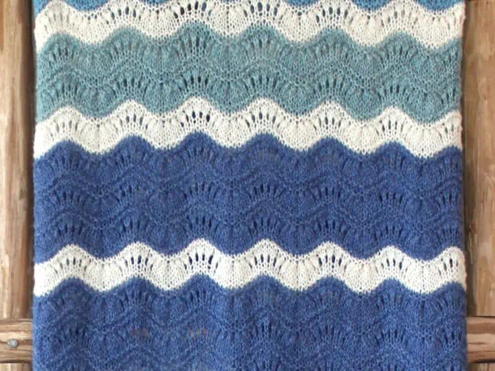 Mavericks Wave Ripple blanket knitted in shades of blue and white displayed on a wooden ladder.
