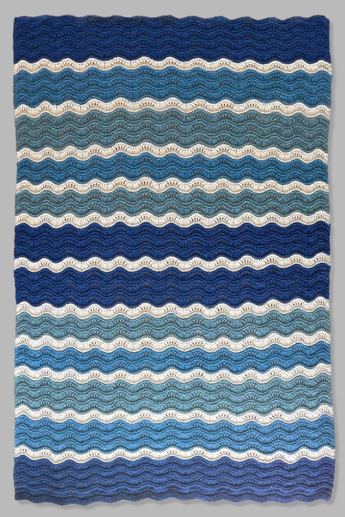 Throw size blanket in full size knitted with shades of blue and white yarn.