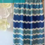 Knitted blanket in ripple wave stitch pattern in shades of blue and white displayed on a wooden ladder.