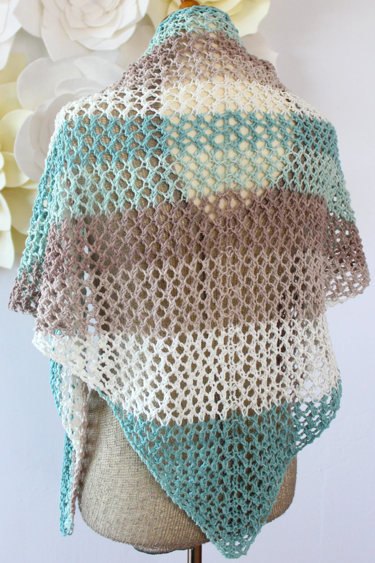 Back view of a triangle shaped knitted mesh shawl in displayed on a mannequin in colors blue, brown, and white.