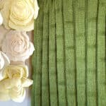 Knitted blanket in bamboo stitch texture in green colored yarn displayed on a wooden ladder.
