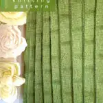 Knitted blanket in bamboo stitch texture in green colored yarn displayed on a wooden ladder.