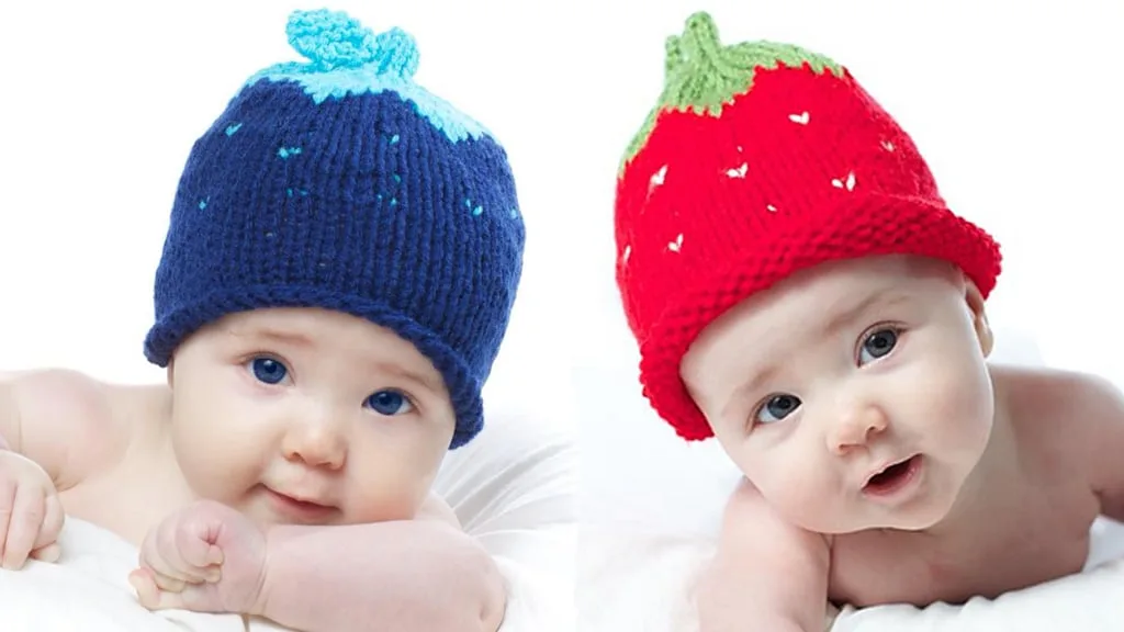 Two babies wearing knitted hats in berry pattern using blue and red yarn colors.