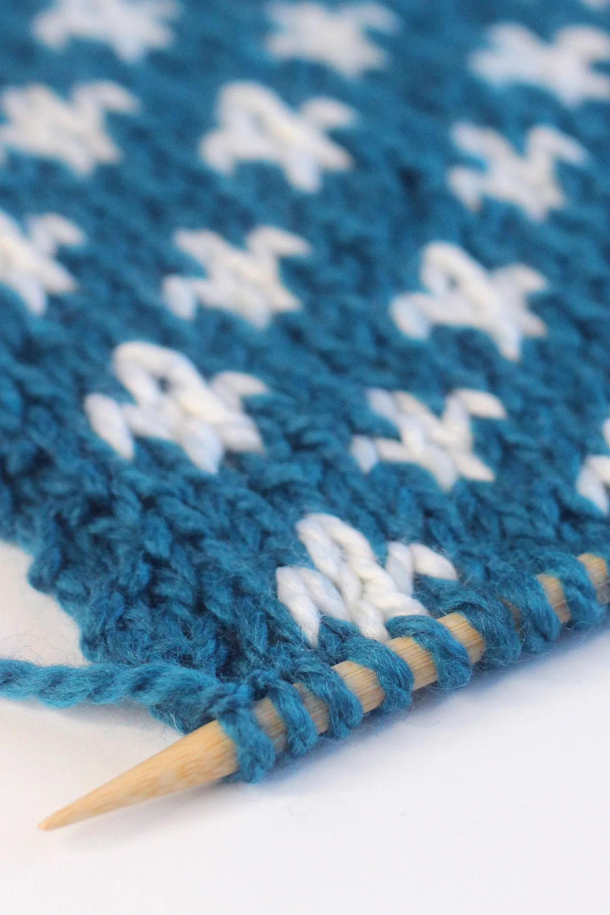 Close-up of Fleur de Lys knit stitch pattern in blue and white color yarn by Studio Knit.