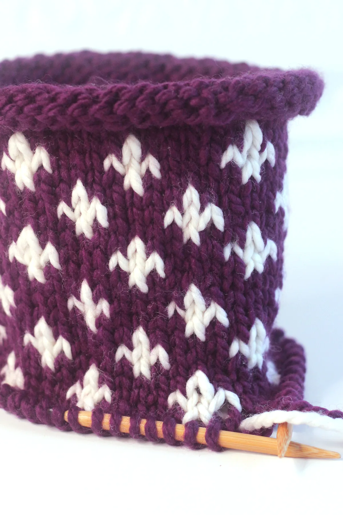 Fleur de Lys knit stitch pattern in purple and white color yarn on circular knitting needle.