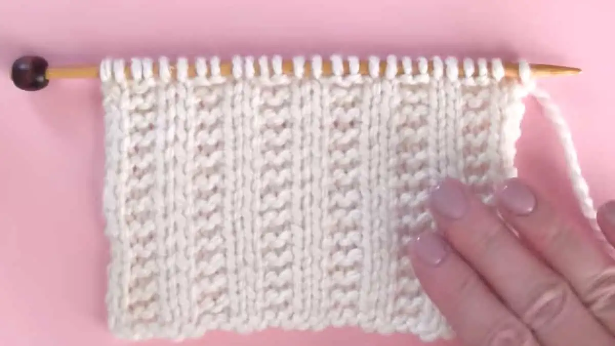 Knitting process with needle, hand, and white colored yarn to create the Garter Ribbing Stitch pattern.