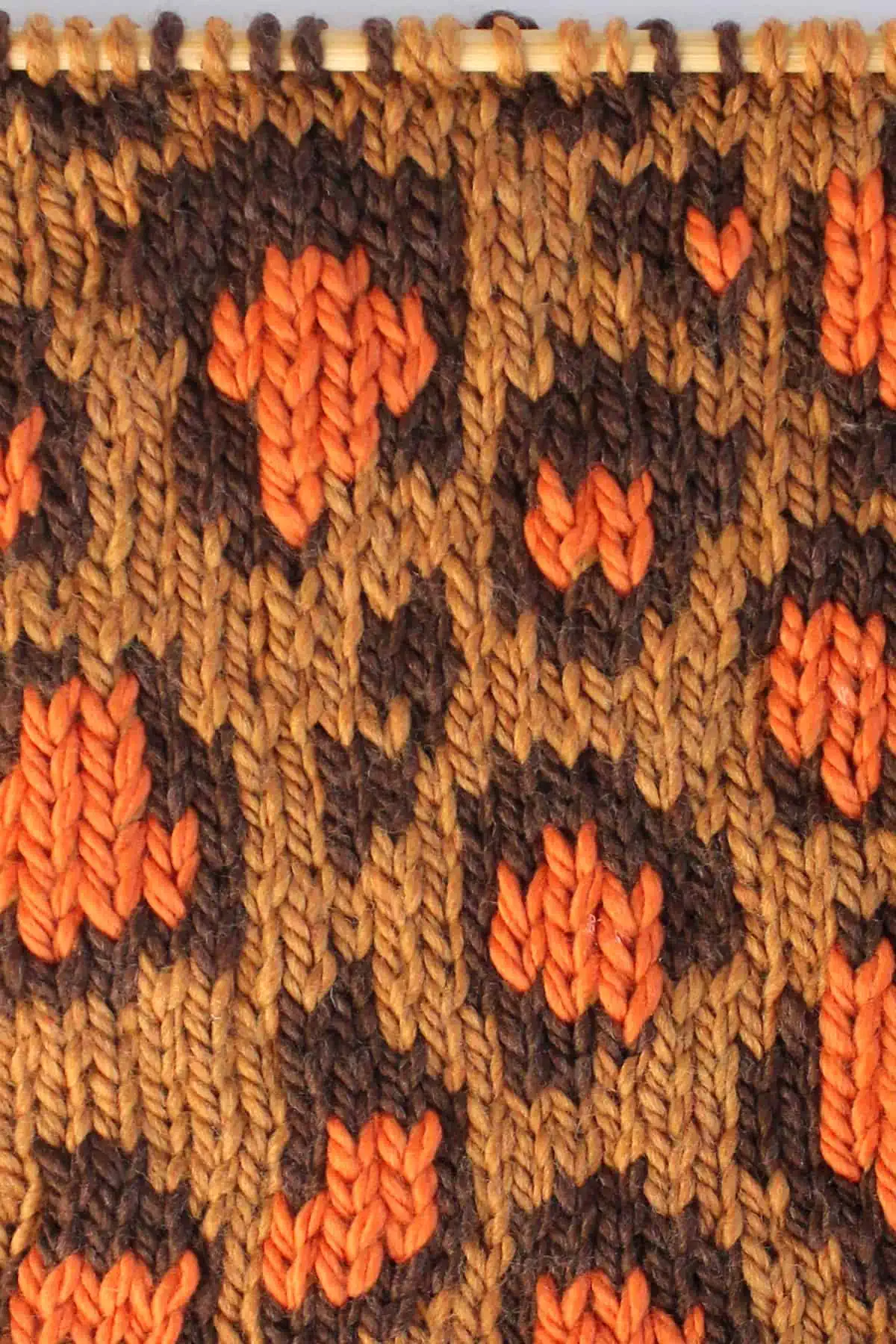 Leopard Print knit stitch stranded colorwork pattern in tan, dark brown, and orange colored yarn on a knitting needle.