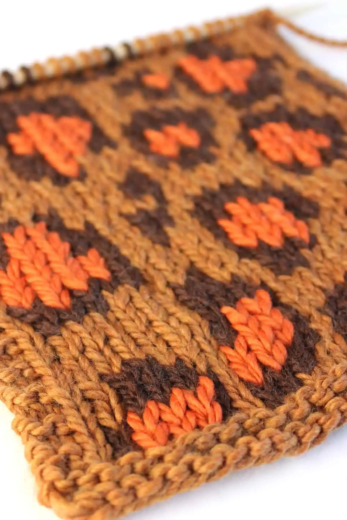 Close-up swatch of the Leopard Print knit stitch pattern in tan, dark brown, and orange colored yarn on a knitting needle.