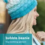 Bubble Beanie knitted hat in shades of blue and white yarn colors topped with a pompom worn by a woman with long blonde hair.