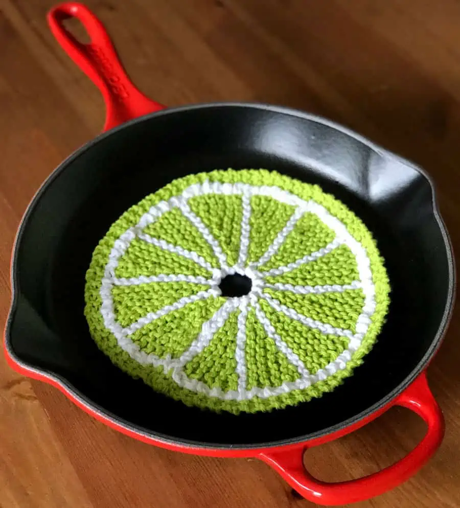 Knitted green fruit slice dishcloth within a kitchen skillet.