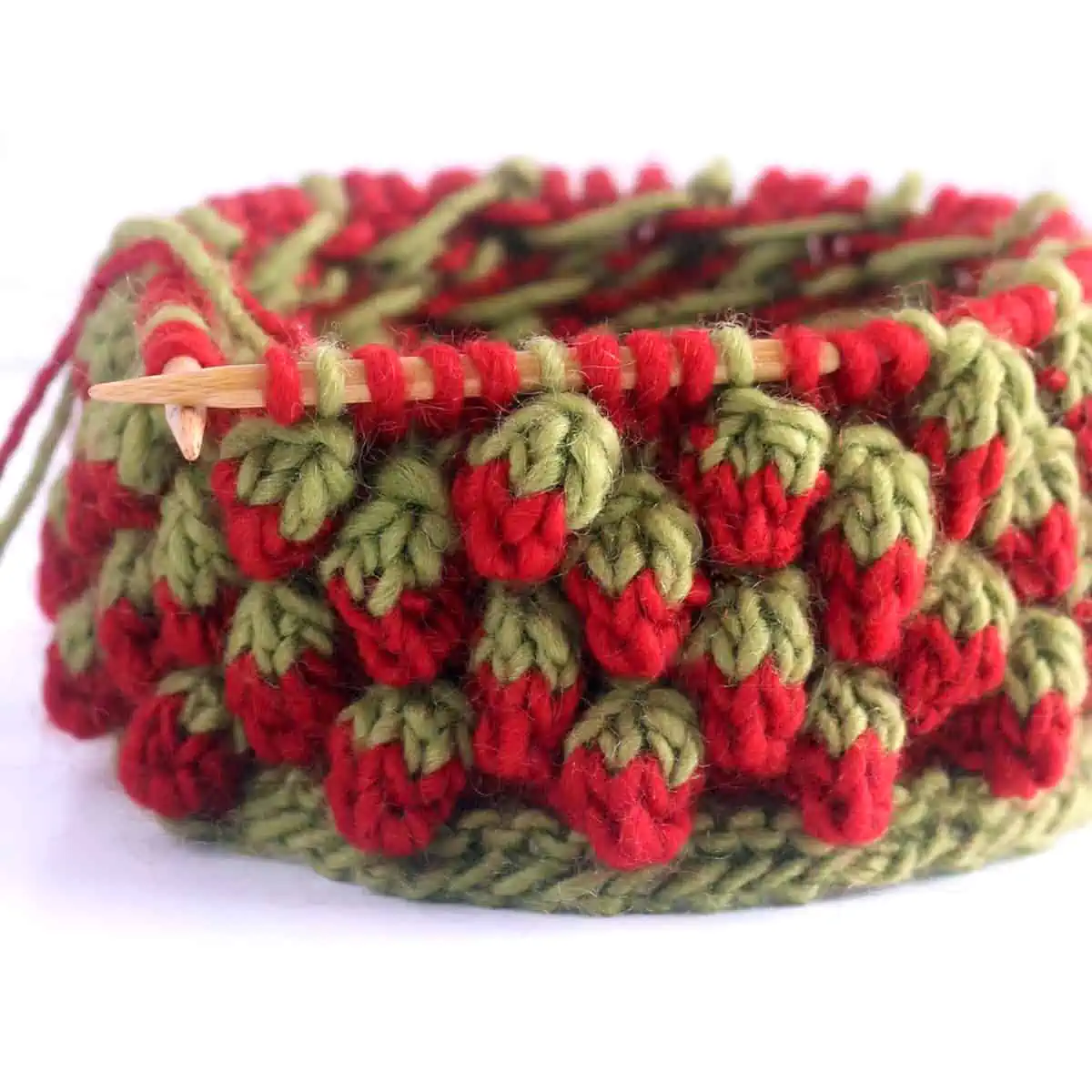 Strawberry bobble stitch knitted in red and green yarn colors on a bamboo circular knitting needle.