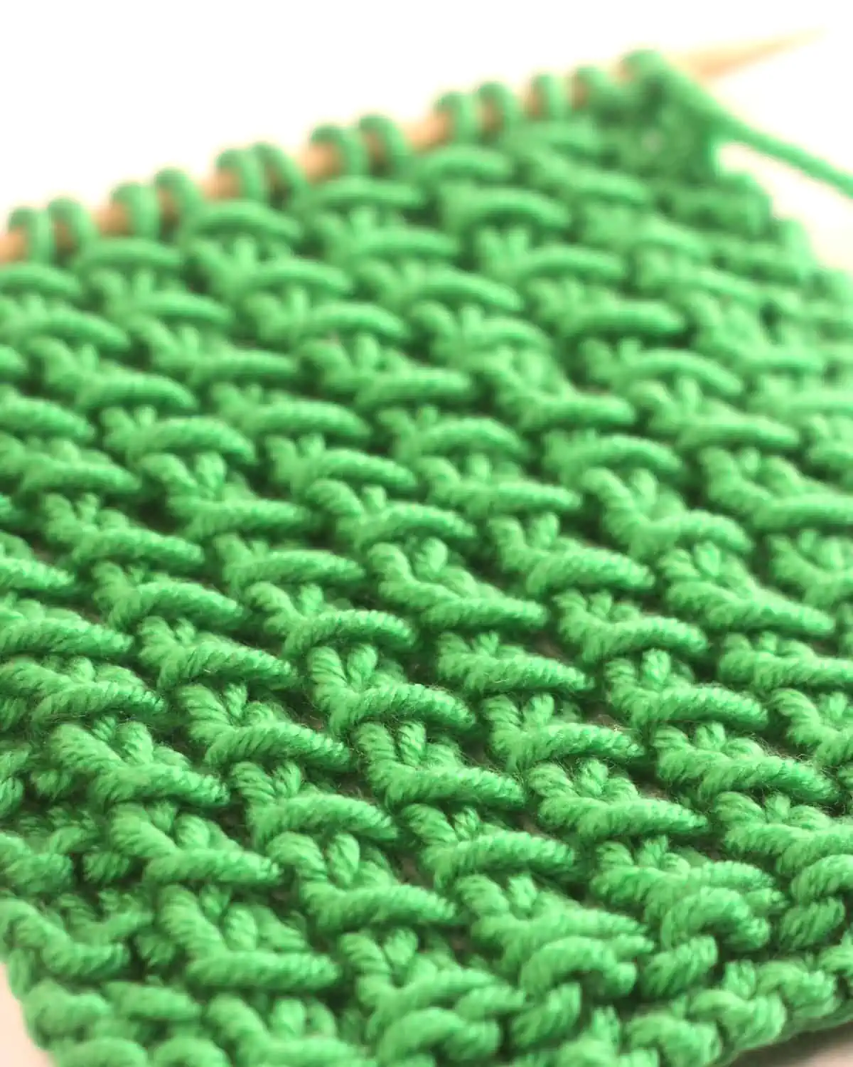 Close-up of the Bamboo Stitch texture knitted with green colored yarn on wooden needle.