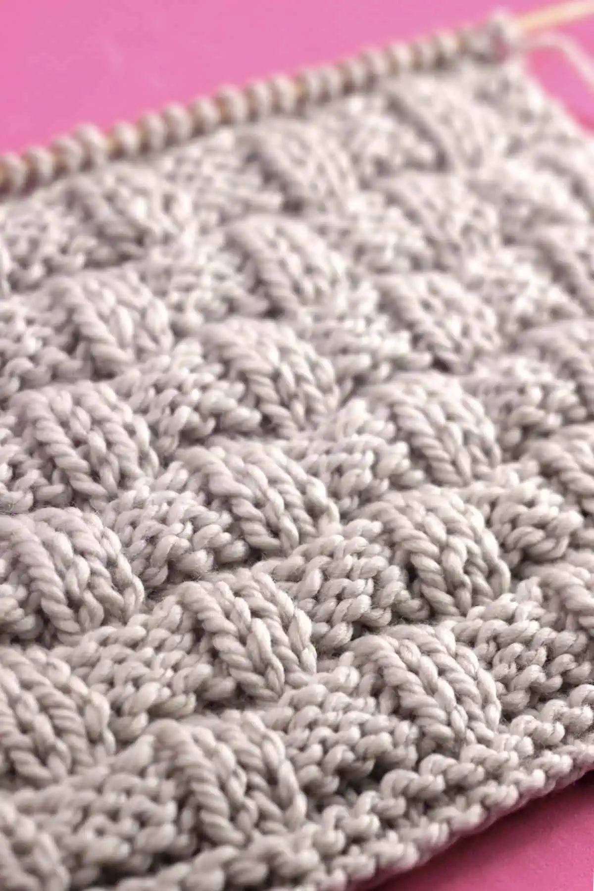 Close-up of the Basket Weave Stitch texture in beige colored yarn on knitting needle.