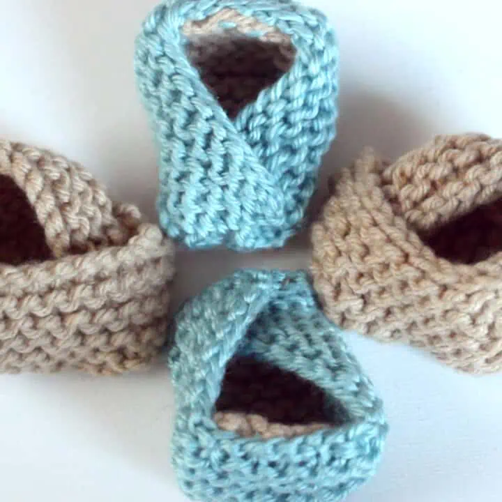 Knitted baby booties in garter stitch with beige and blue yarn colors.