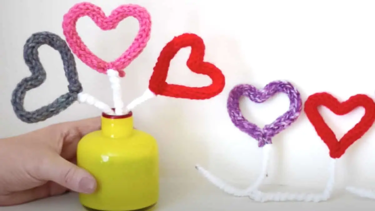 Knitted hearts arranged in a yellow vase with hand.