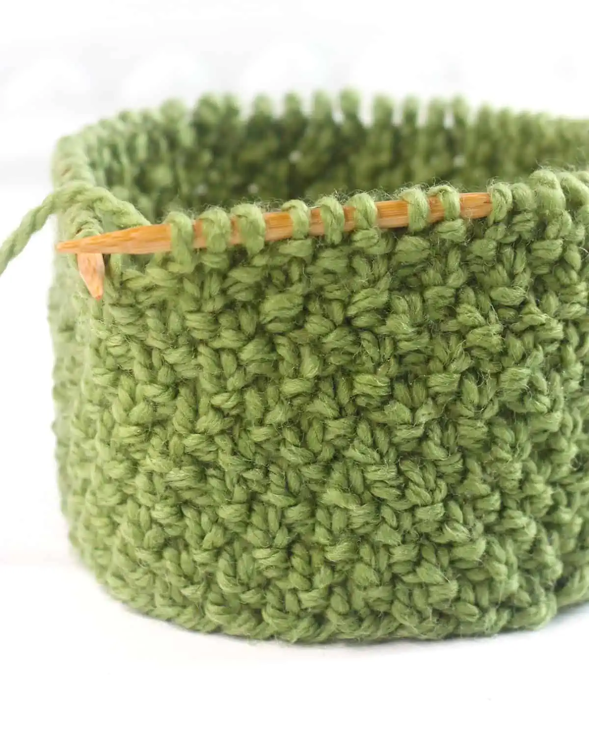 Irish Moss knit stitch pattern texture on circular wooden needle in green yarn color.