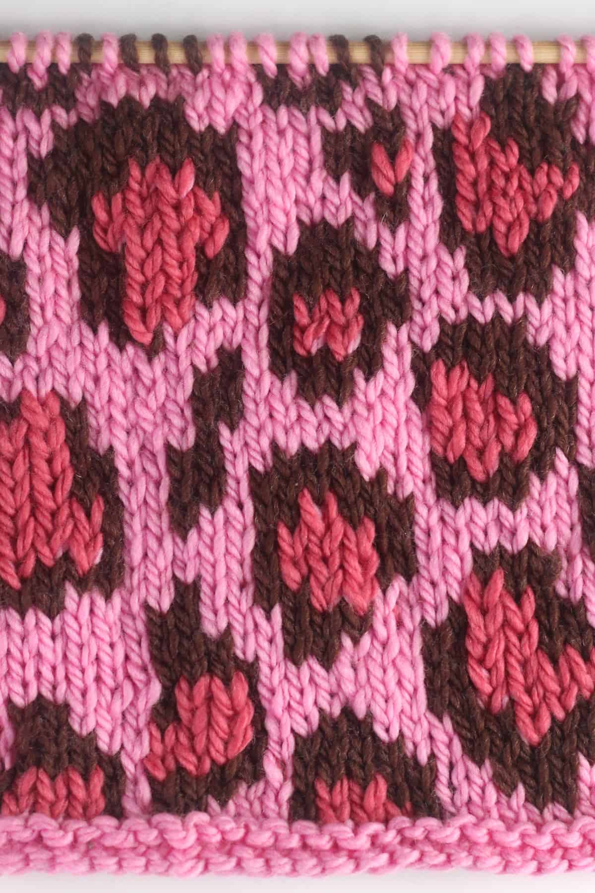 Leopard Print knit stitch stranded colorwork pattern in shades of pink and brown colored yarn on a knitting needle.