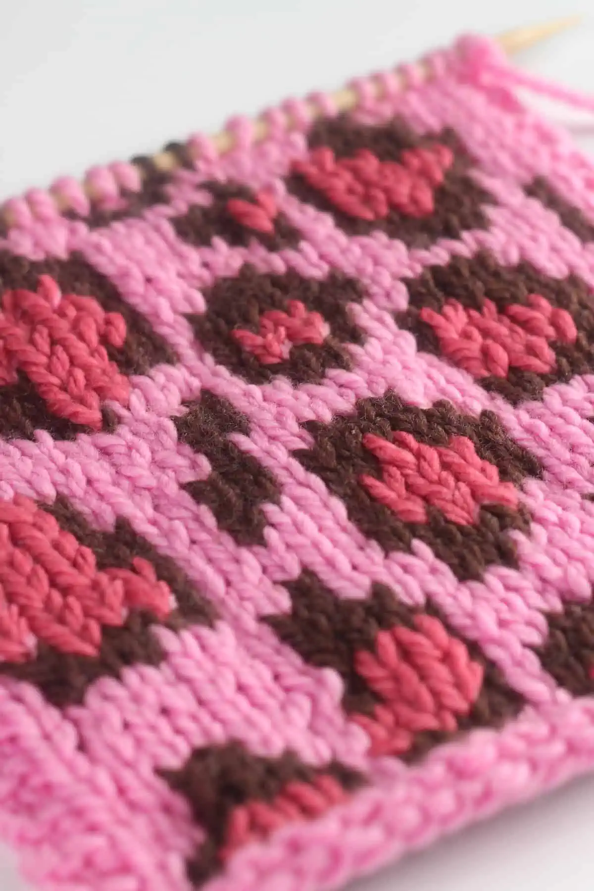 Close-up swatch of the Leopard Print knit stitch pattern in shades of pink and brown colored yarn on a knitting needle.