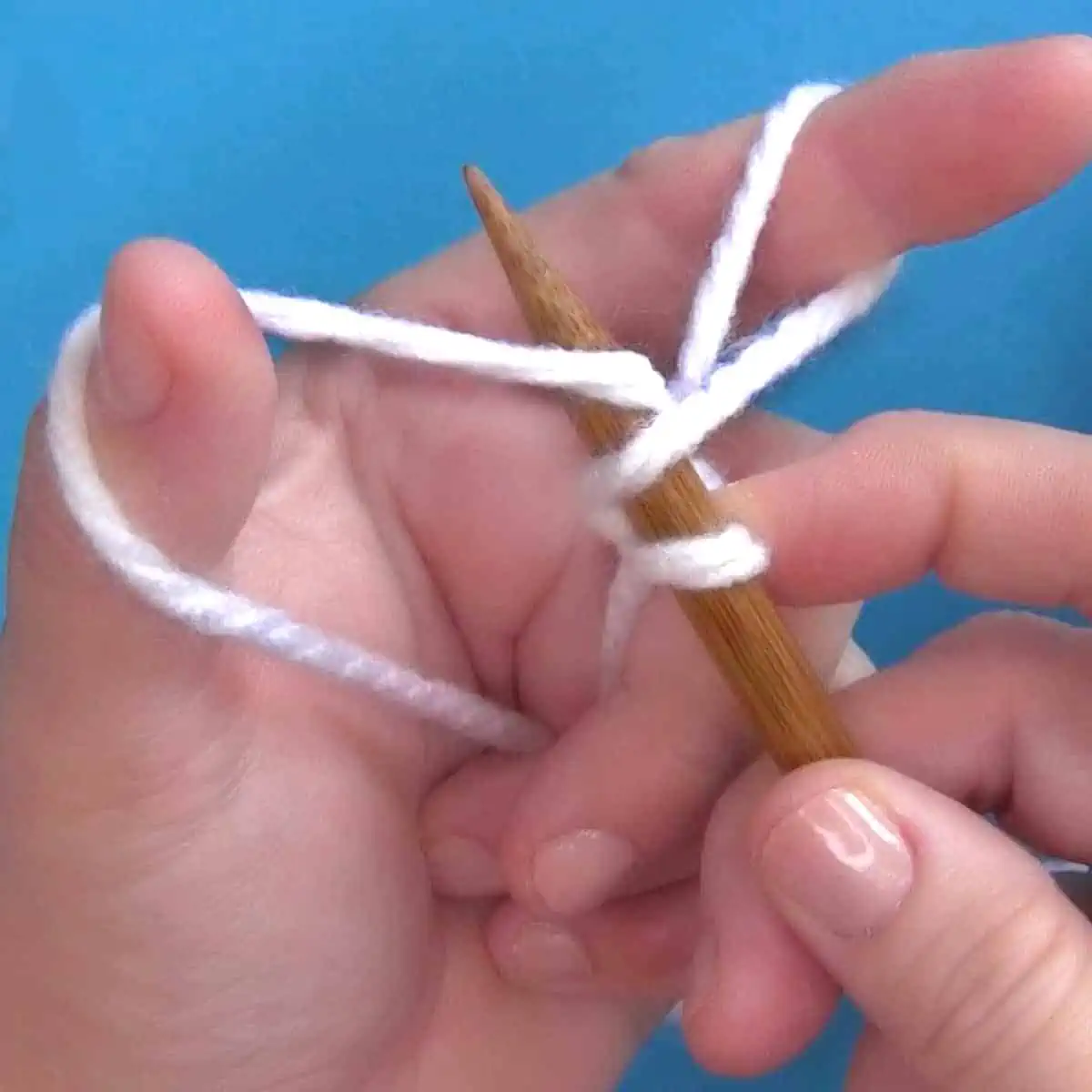 Hands demonstrating How to Long Tail Cast On Purlwise with yarn and knitting needles.