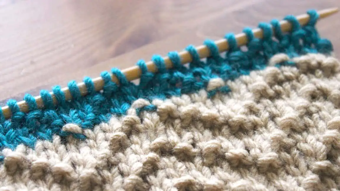 Chevron Seed stitch knitted with beige and blue colored yarn on wooden knitting needle.
