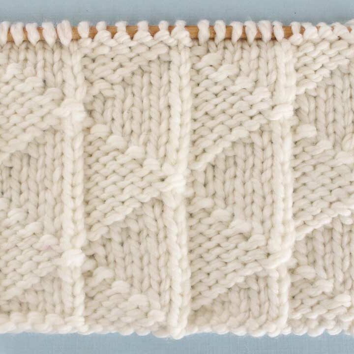 Knitting texture with Pennant Pleating stitch in white colored yarn on needle.