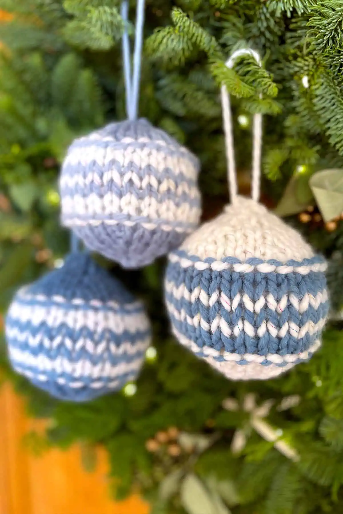 Knitted Christmas Balls in blue and white yarn colors hanging from greenery.