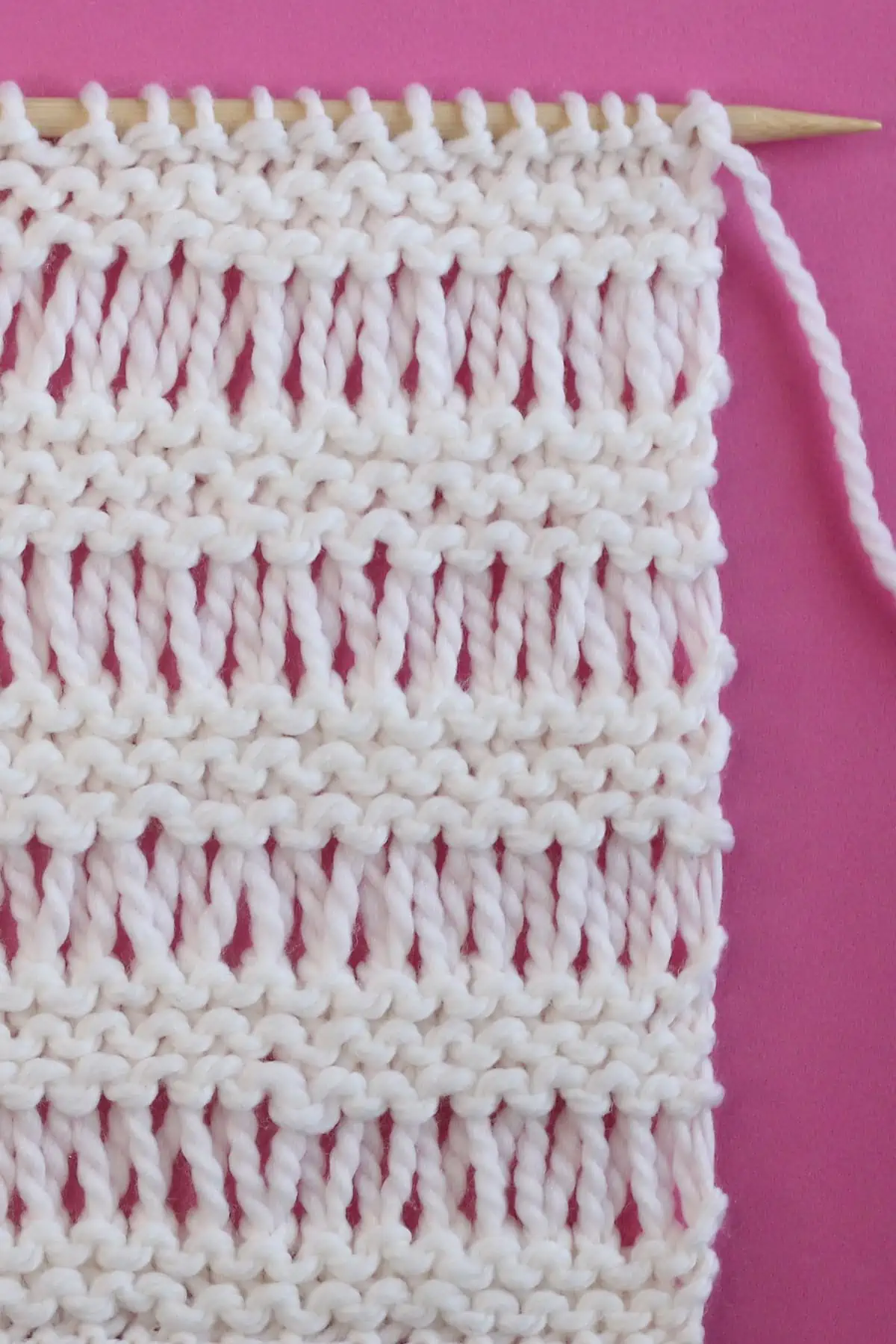 Garter Drop Stitch knitting texture in white yarn color on a wooden needle.