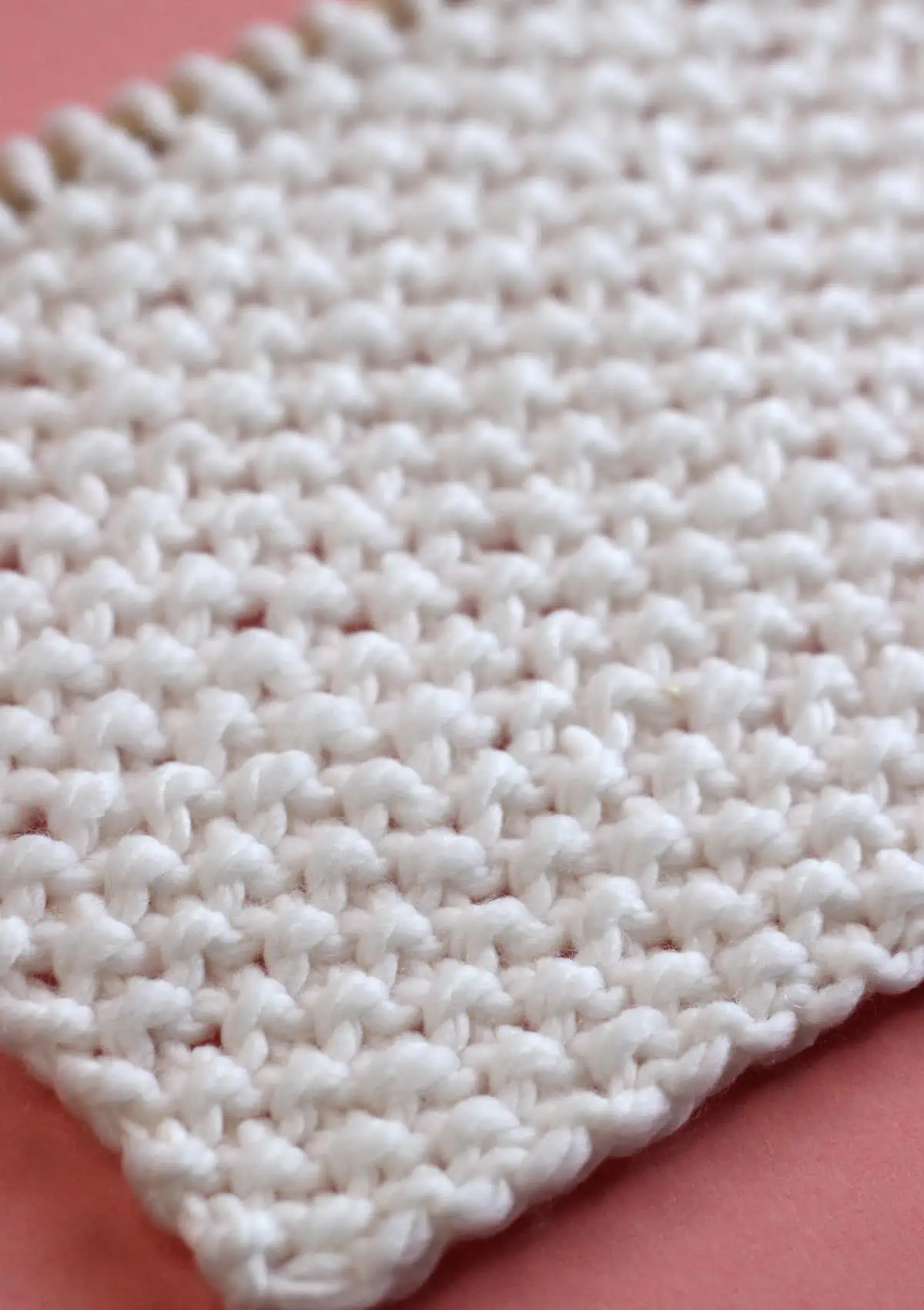 Seed Stitch knitting texture in white yarn color on a wooden needle.