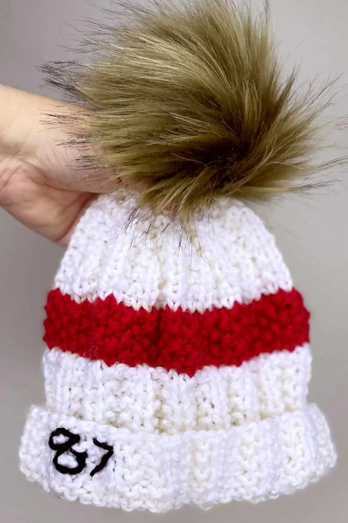 Hand holiding the white and red knitted Taylor Swift's 87 Beanie Hat.