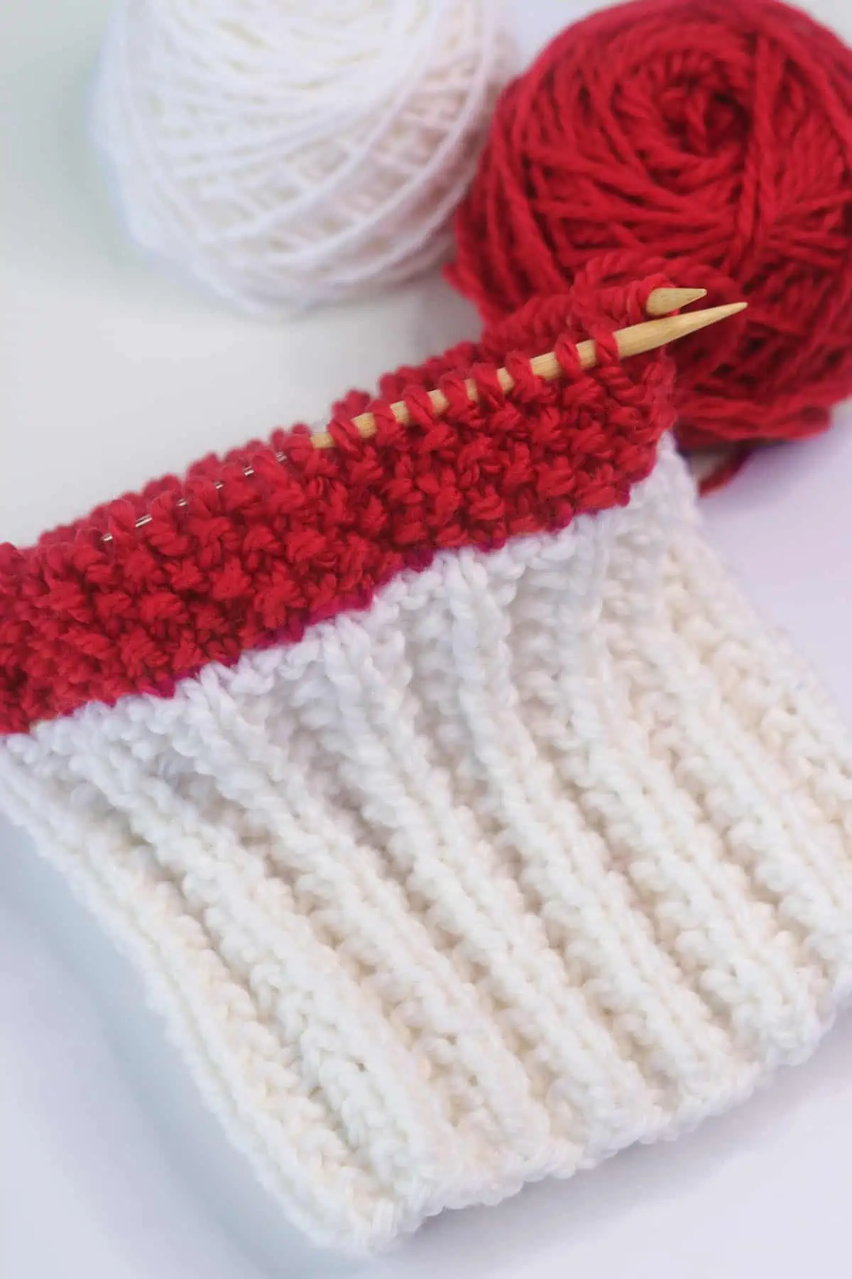 Knitting process of the Sideline Spirit ribbed hat on a circular needle with red and white yarn colors.