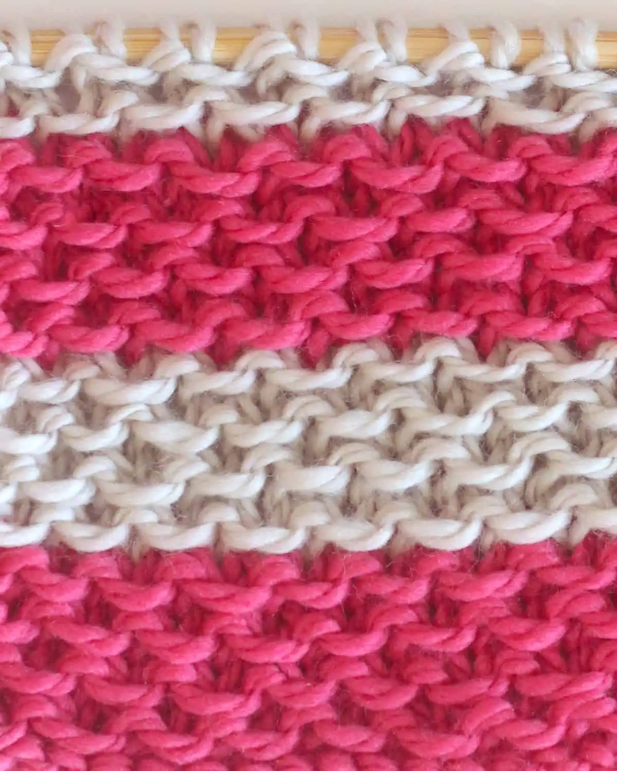 Color changes of the Stamen Knit Stitch in pink and beige colored yarn on knitting needles.
