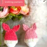 Bunny Egg Cozy knitting pattern by Studio Knit in peach and pink yarn colors beside a llama toy and flower vase.