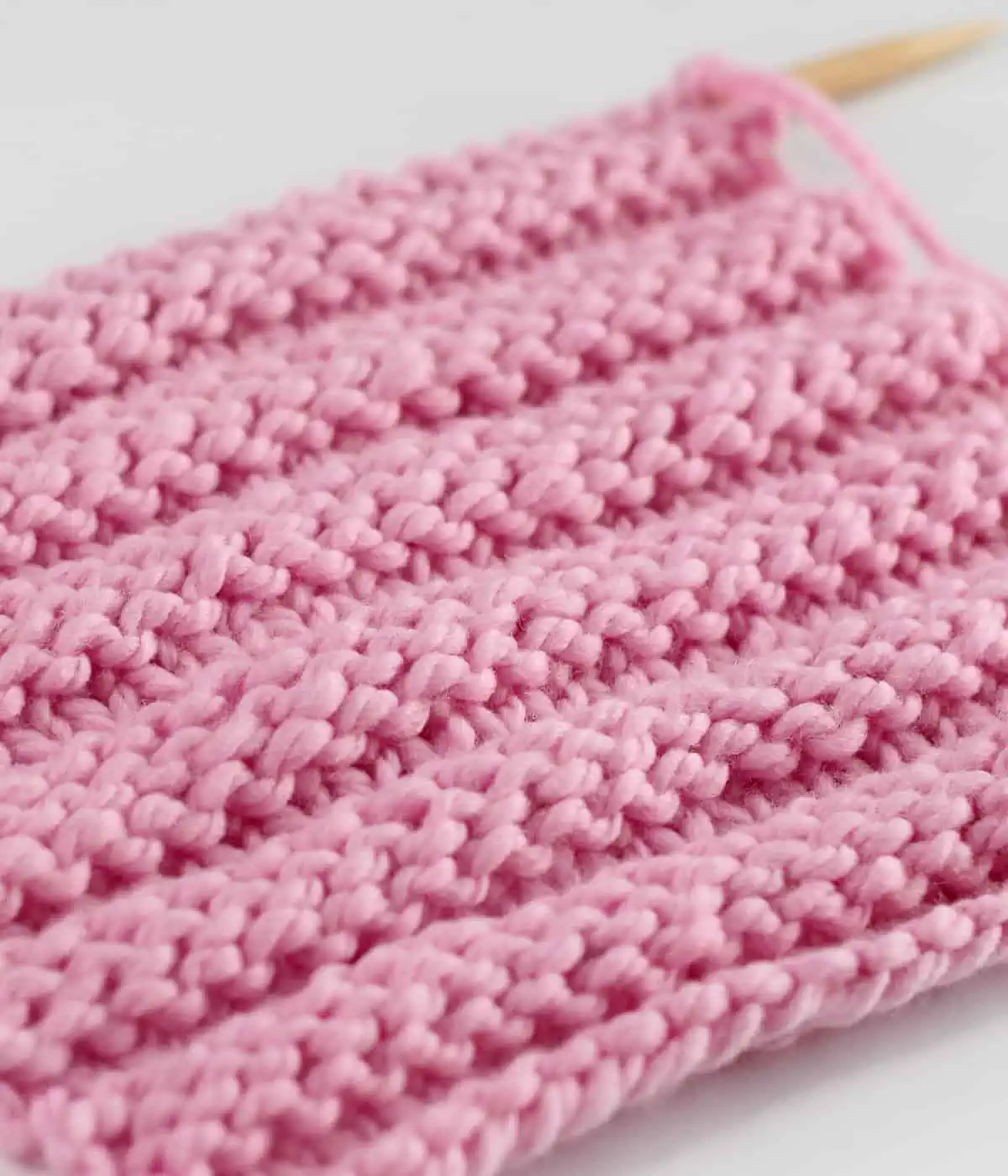 Reverse Ridge knit stitch texture in pink yarn color on wooden needle.