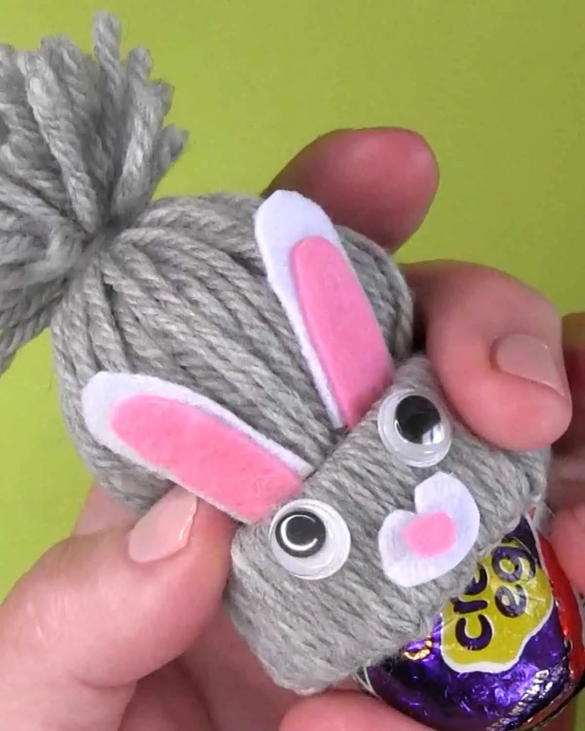 Hands inserting a Cadbury Creme Egg into a Yarn Craft Bunny Cover.