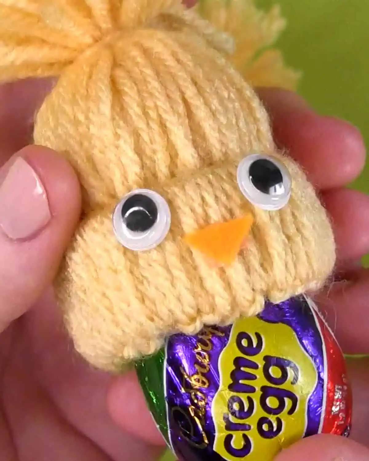 Hands inserting a Cadbury Creme Egg into a Yarn Craft Chick Cover.