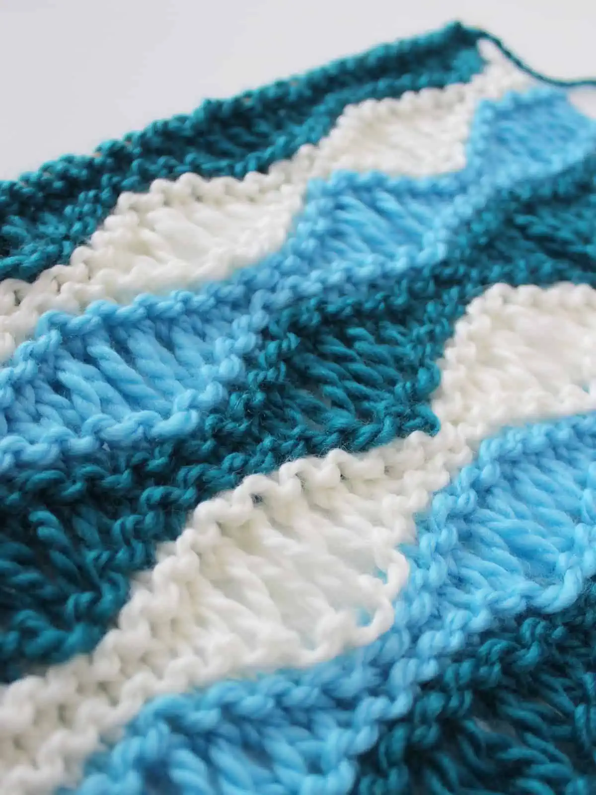 Close-up side view of the Sea Foam Wave Drop Stitch Knitting Pattern in dark blue, light blue, and white yarn colors.