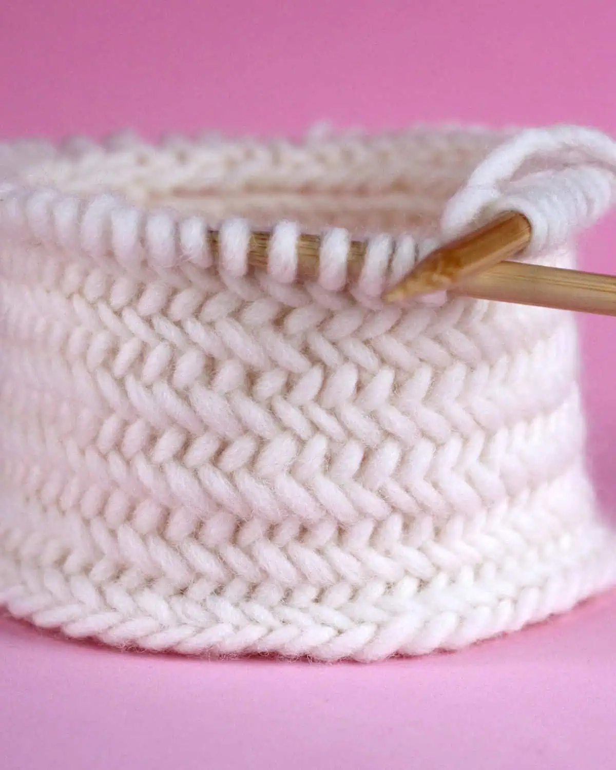 Herringbone knit stitch texture in white colored yarn on circular needles.