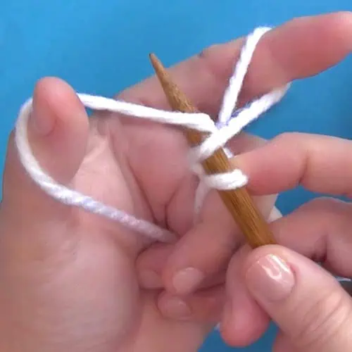 Hands demonstrating How to Long Tail Cast On Purlwise with yarn and knitting needles.