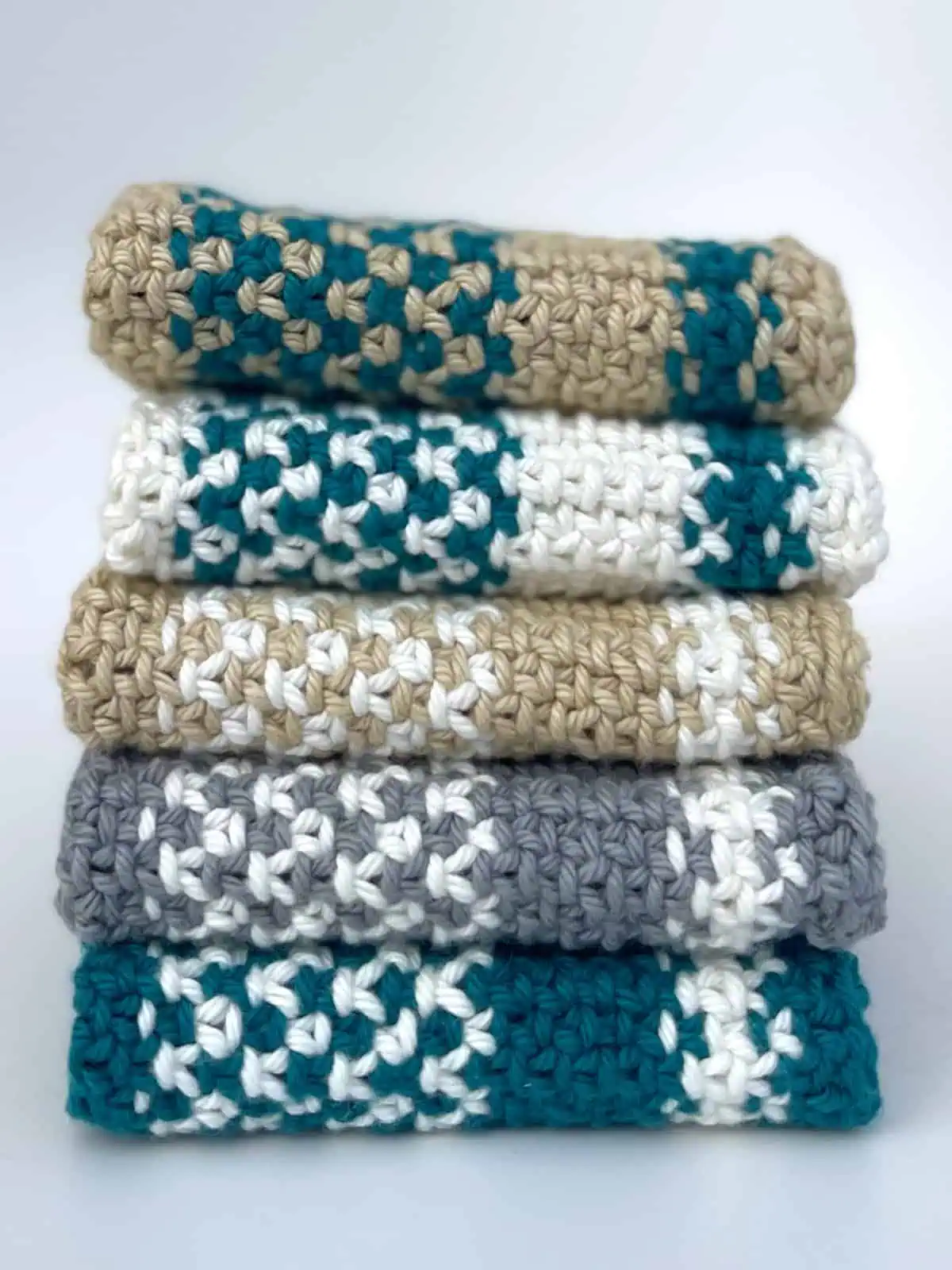 Stack of five knitted dishcloths in the linen stitch with blue, white, grey, and tan yarn colors.